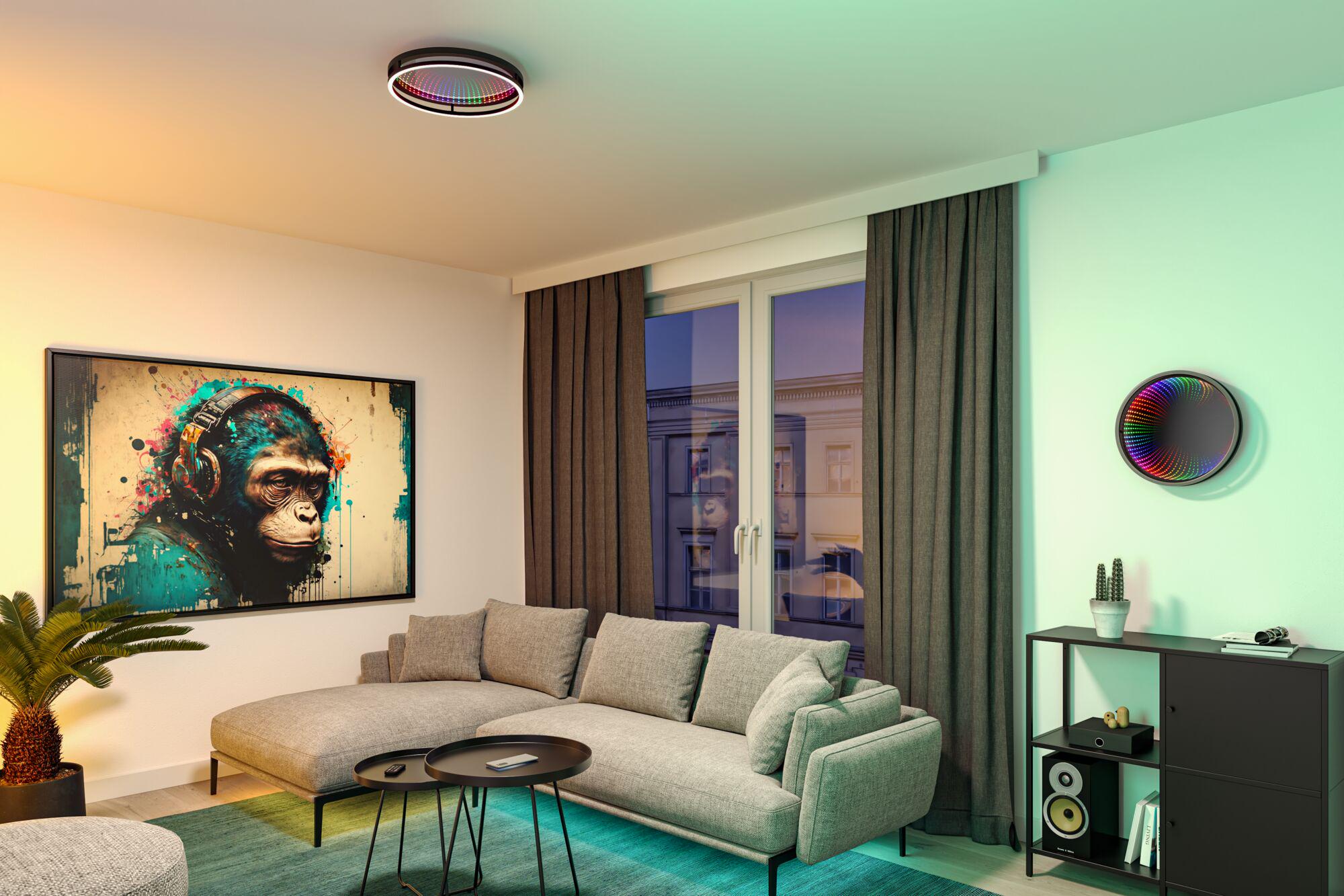 Modernes Wohnzimmer mit grauem Stoffsofa, schwarzem Regal und bunter LED-Deckenleuchte von Paulmann.