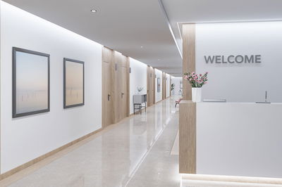 Hall d'accueil moderne avec comptoir blanc, détails en bois et éclairage LED au plafond dans un couloir.