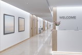 Hall d'accueil moderne avec comptoir blanc, détails en bois et éclairage LED au plafond dans un couloir.