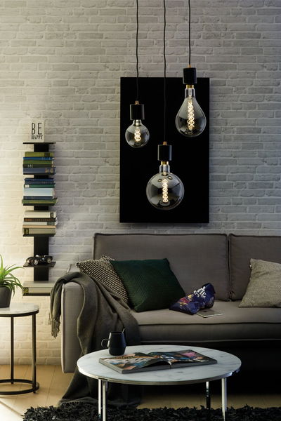 Three LED filament bulbs with smoke glass hanging above grey sofa in modern living room with bookshelf.