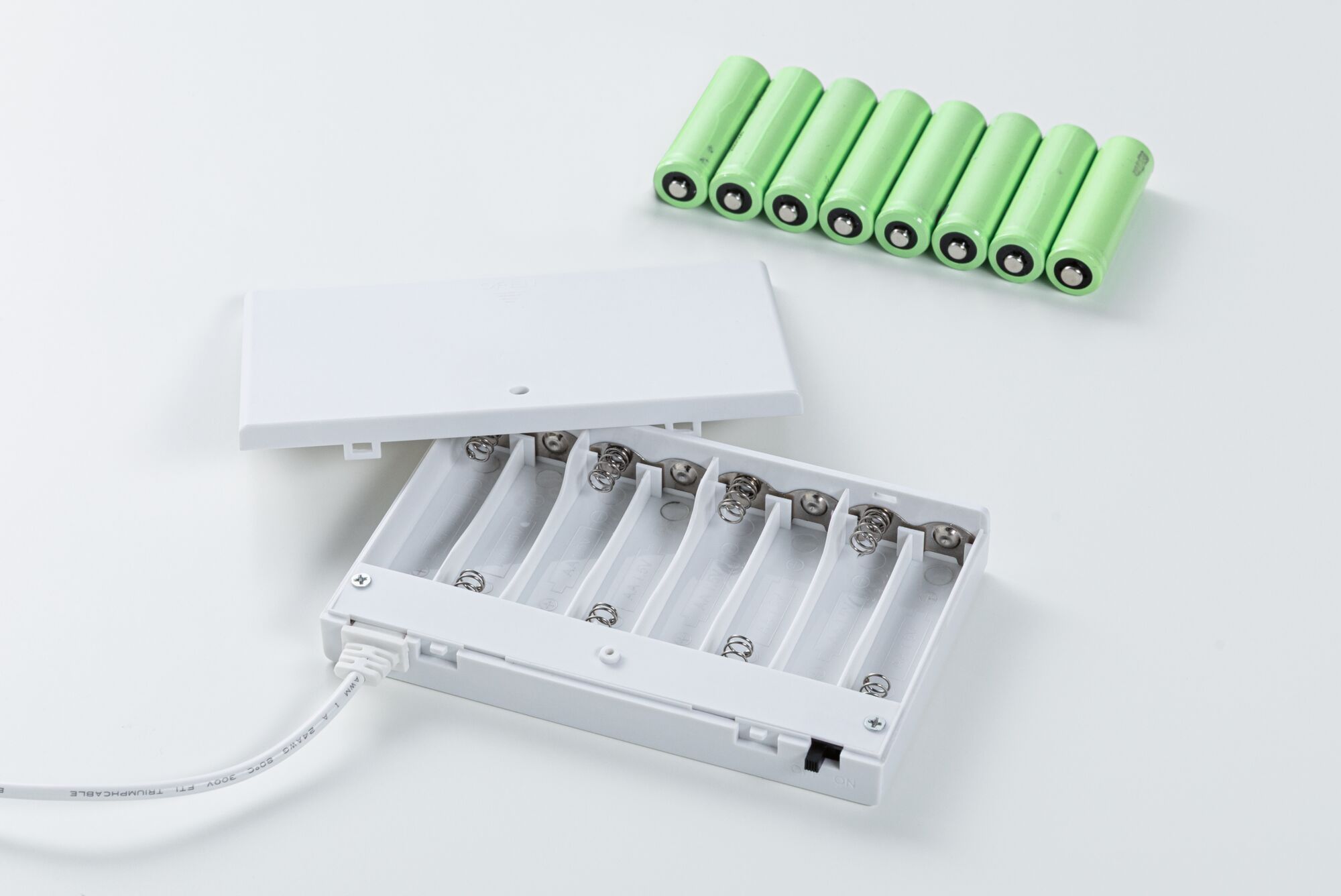 Boîtier à piles blanc ouvert avec huit piles rechargeables AA vertes sur fond blanc