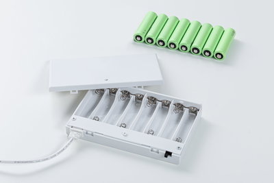 Boîtier à piles blanc ouvert avec huit piles rechargeables AA vertes sur fond blanc