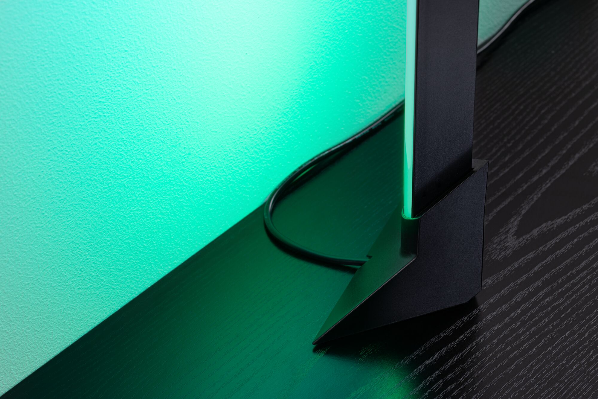 Black LED floor lamp with green light on dark wood table for modern room lighting