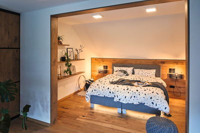 Chambre moderne avec sol en bois, lit gris et éclairage LED blanc chaud au plafond pour une ambiance cosy
