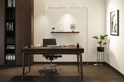 Moderne kantoorruimte met donkerhouten bureau, zwarte leren stoel en witte LED-railverlichting aan de muur.