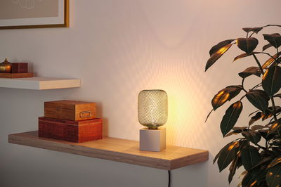 Moderne tafellamp met grijze metalen kubusvoet en decoratieve draadkap die warm licht verspreidt