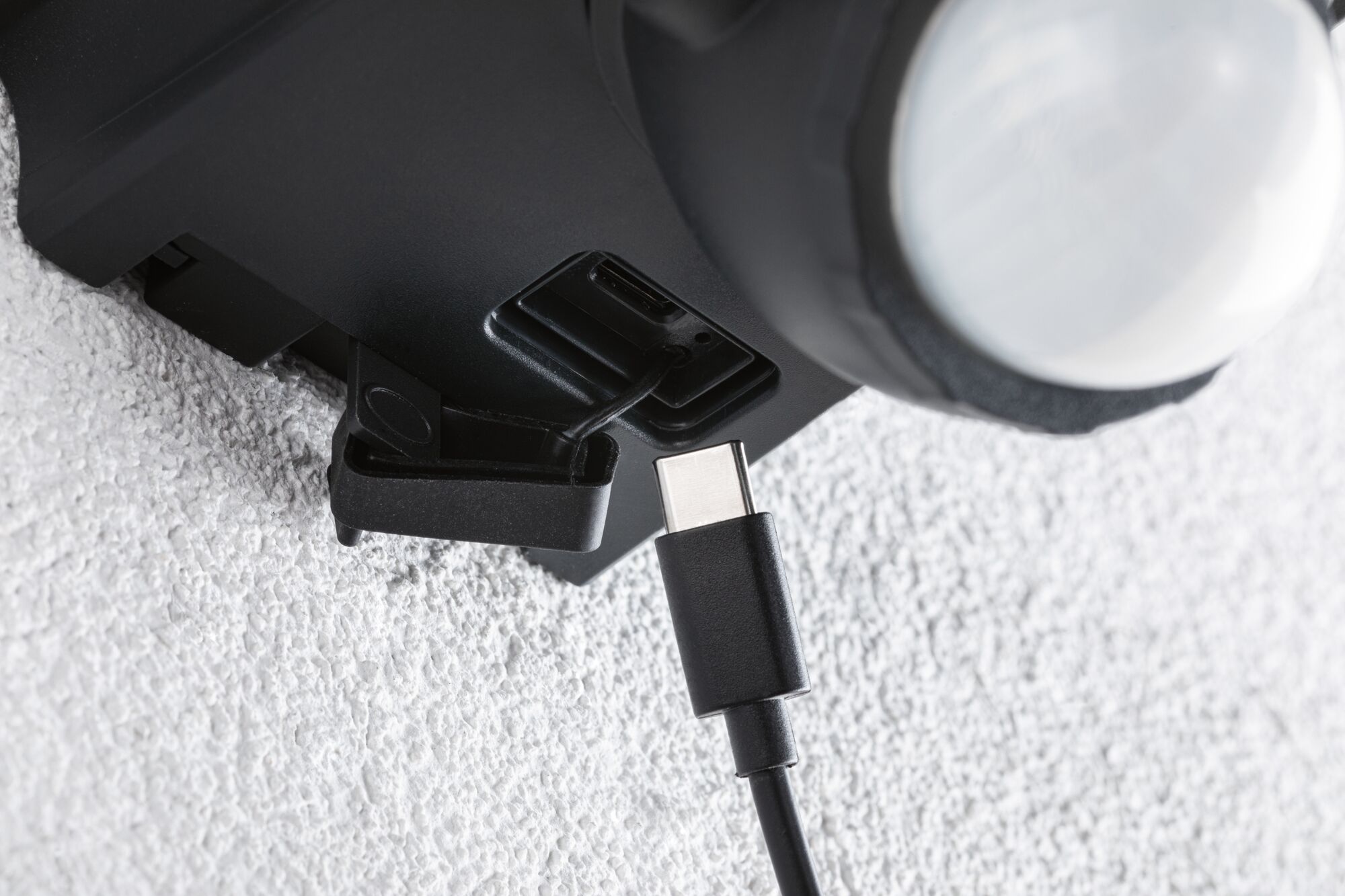 Nahaufnahme eines schwarzen USB-C-Kabels, das in einen schwarzen Anschluss an einem Gerät eingesteckt wird, Texturierte weiße Wand im Hintergrund