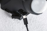 Nahaufnahme eines schwarzen USB-C-Kabels, das in einen schwarzen Anschluss an einem Gerät eingesteckt wird, Texturierte weiße Wand im Hintergrund