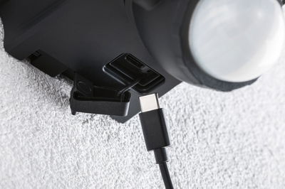 Nahaufnahme eines schwarzen USB-C-Kabels, das in einen schwarzen Anschluss an einem Gerät eingesteckt wird, Texturierte weiße Wand im Hintergrund