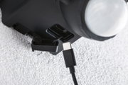 Nahaufnahme eines schwarzen USB-C-Kabels, das in einen schwarzen Anschluss an einem Gerät eingesteckt wird, Texturierte weiße Wand im Hintergrund