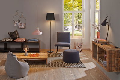 Moderne woonkamer met grijze stoel, poef, houten plank en diverse lampen voor sfeervolle verlichting