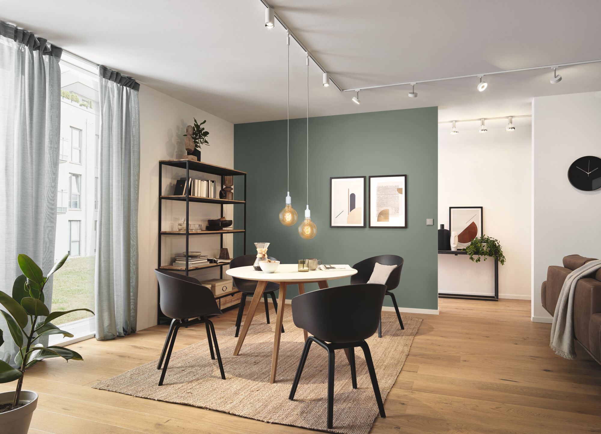 Modern dining area with round wooden table, black chairs, and warm LED pendant lights on track system