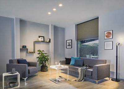 Moderne woonkamer met grijze stoffen bank, fauteuil, witte bijzettafel en dimbare LED-plafondspots.