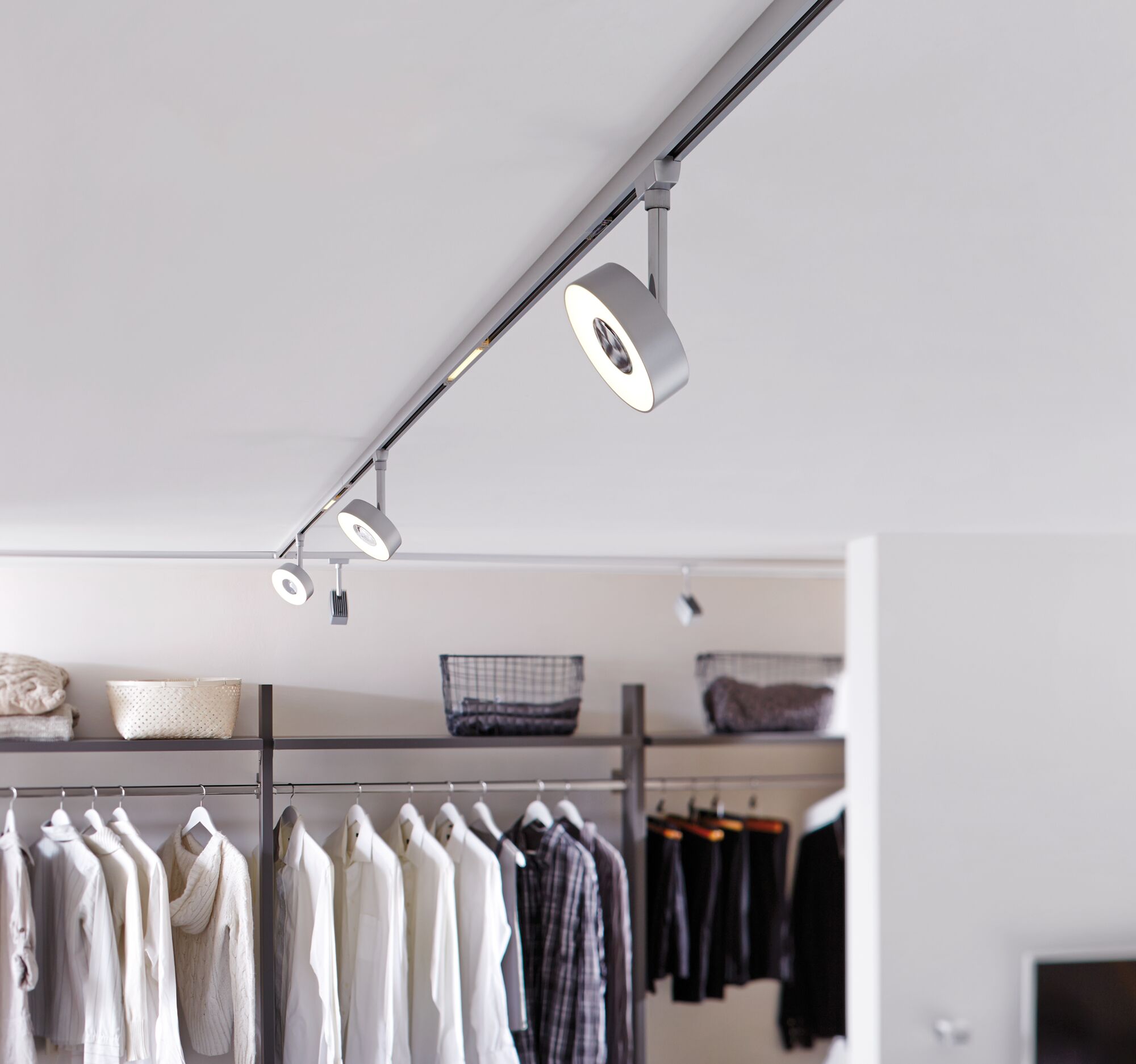 Modern white metal LED track spotlight in dressing room with clothes and storage baskets