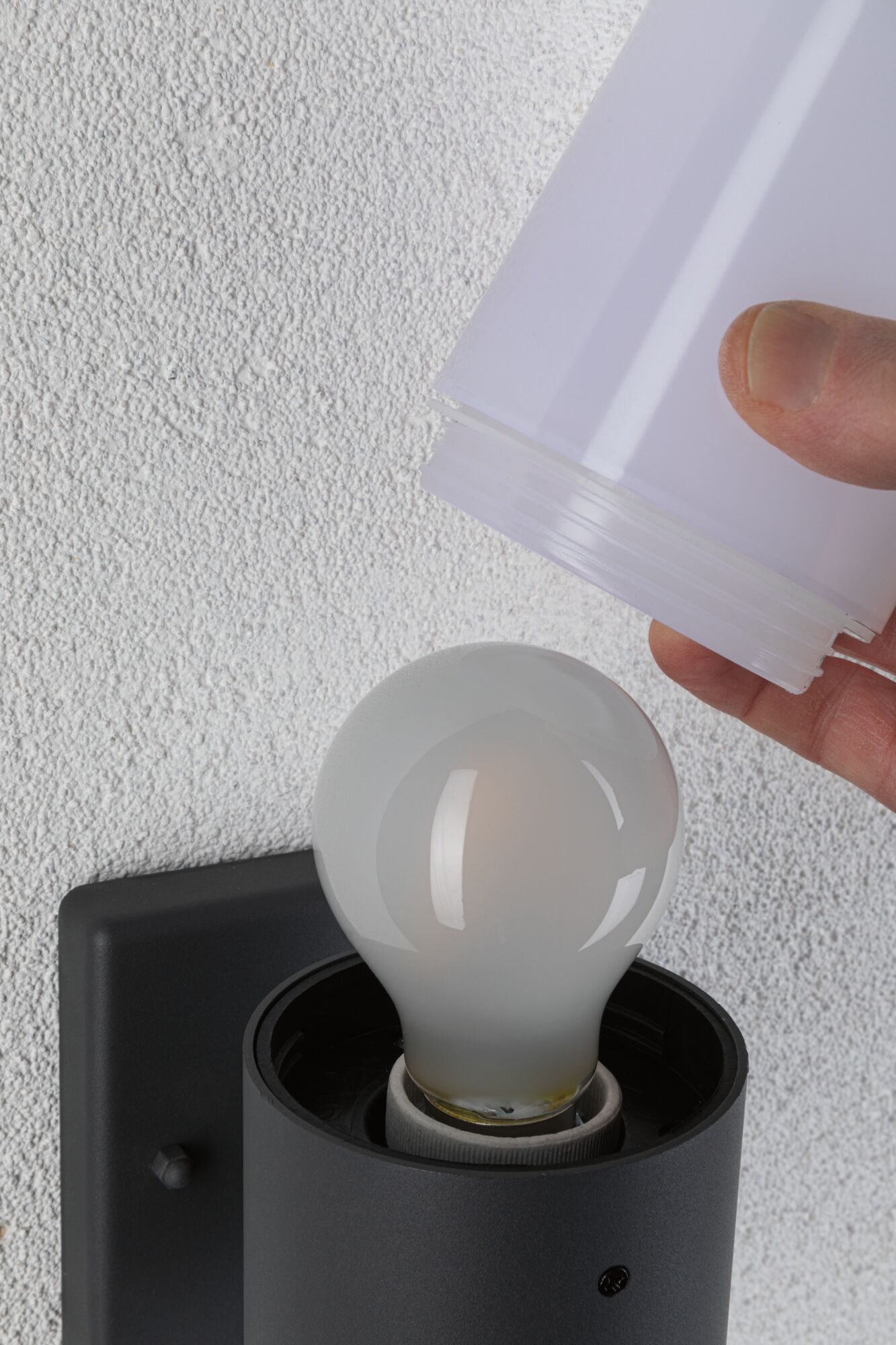 Hand hält weißen Lampenschirm aus Kunststoff über matte Glühbirne in schwarzer Wandlampe