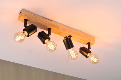 Deckenstrahler mit vier schwarzen Metalllampen an Holzleiste, warmweißes LED-Licht für Wohnraum.
