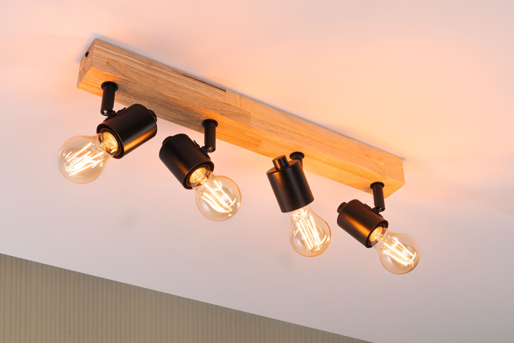 Deckenstrahler mit vier schwarzen Metalllampen an Holzleiste, warmweißes LED-Licht für Wohnraum.