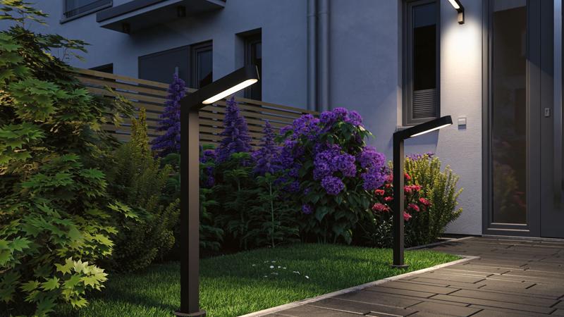 Lampadaires noirs modernes en métal éclairant un chemin de jardin avec fleurs colorées et façade de maison.