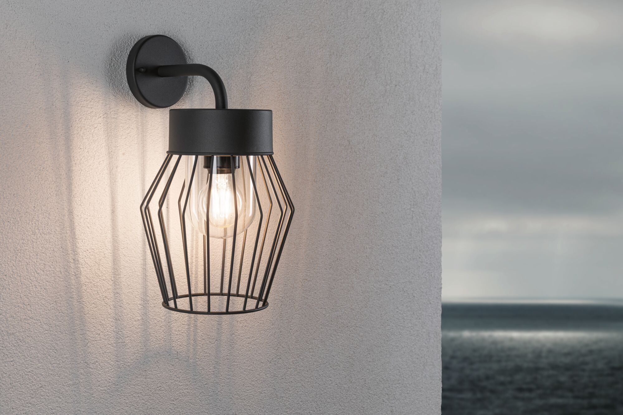 Black metal wall lamp with cage design and visible bulb, modern outdoor lighting fixture.