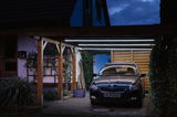 Carport mit Holzrahmen und LED-Röhrenbeleuchtung bei Nacht, modernes Außenlicht für Haus und Auto
