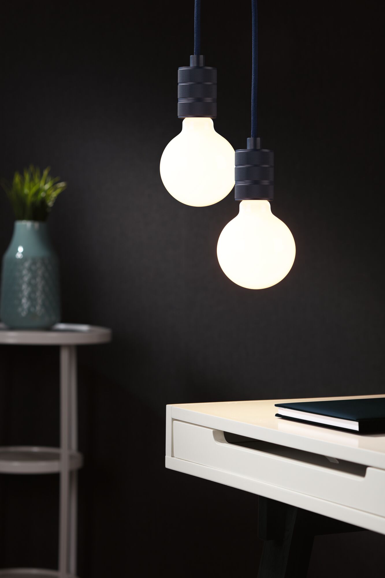 Two round LED pendant lights with matte black holders above white desk with book.