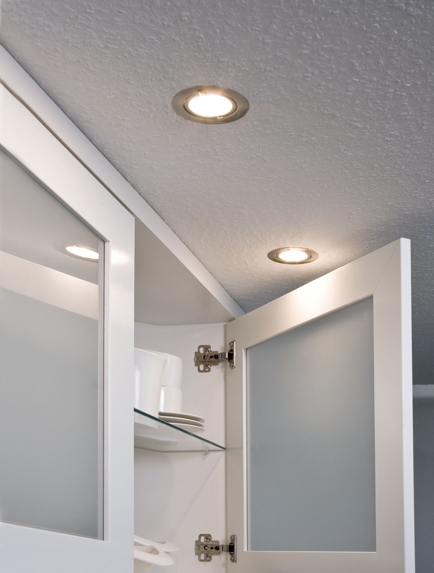 Twee ronde inbouwspots met warm wit licht in witte keuken met open kast.