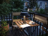 Modern black metal table lamp on wooden balcony table with book and tea cup in evening light