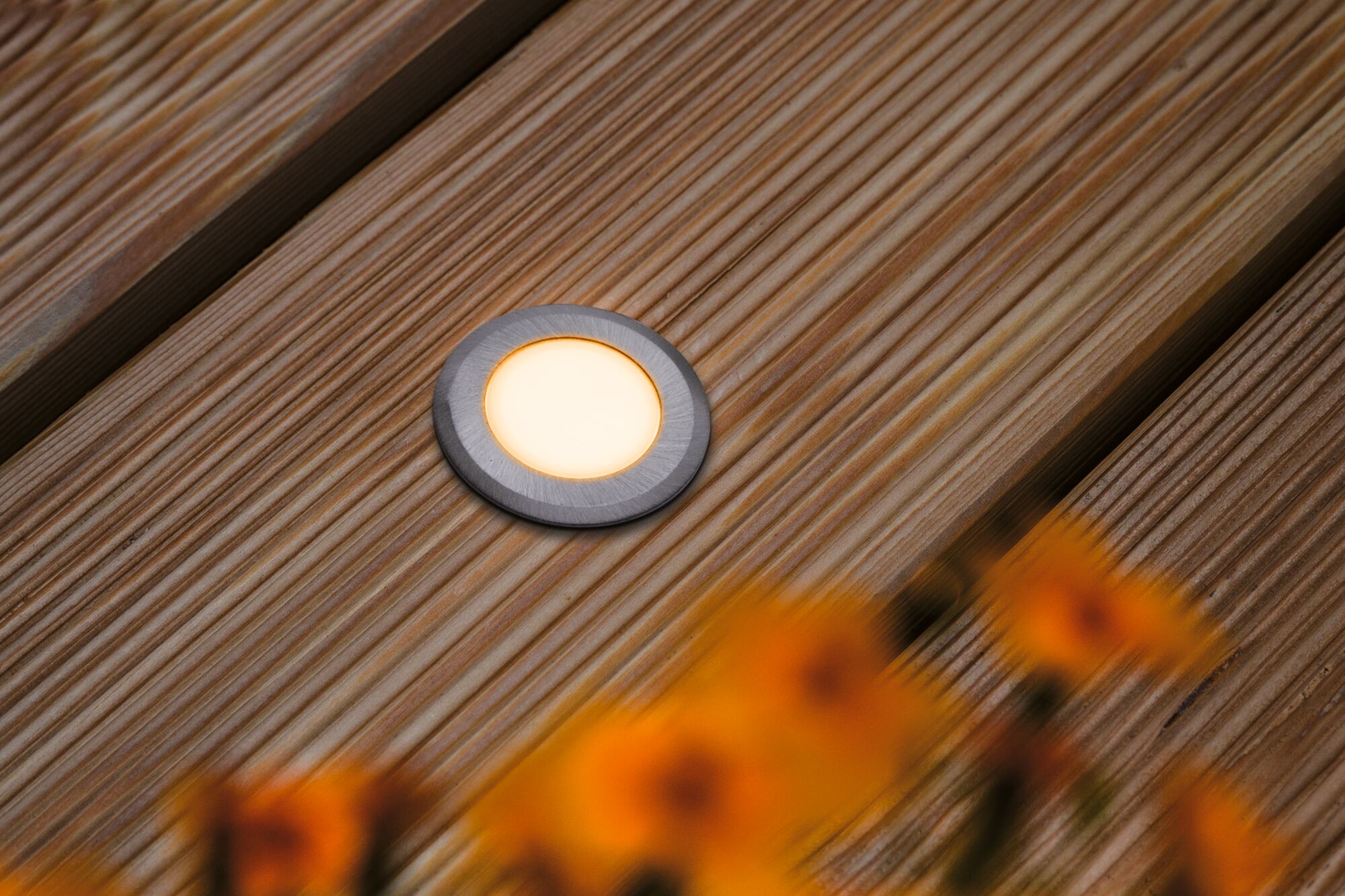 Ronde LED inbouwvloerlicht in geborsteld aluminium op houten terras met warm wit licht.