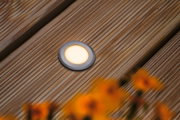 Lumière LED encastrée ronde en aluminium brossé sur terrasse en bois avec éclairage blanc chaud.