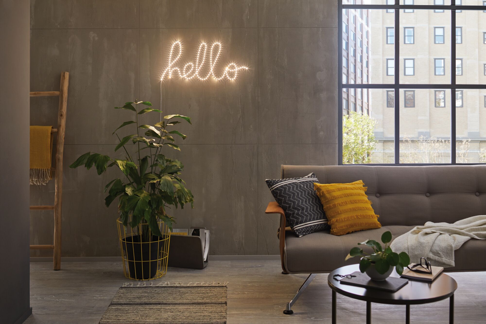 Modernes Wohnzimmer mit grauer Couch, gelben Kissen, grüner Pflanze und LED-Wandlicht 'hello' für Wohnraumbeleuchtung