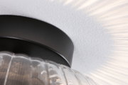 Ceiling light with black metal ring and ribbed clear glass, warm light casting shadow patterns