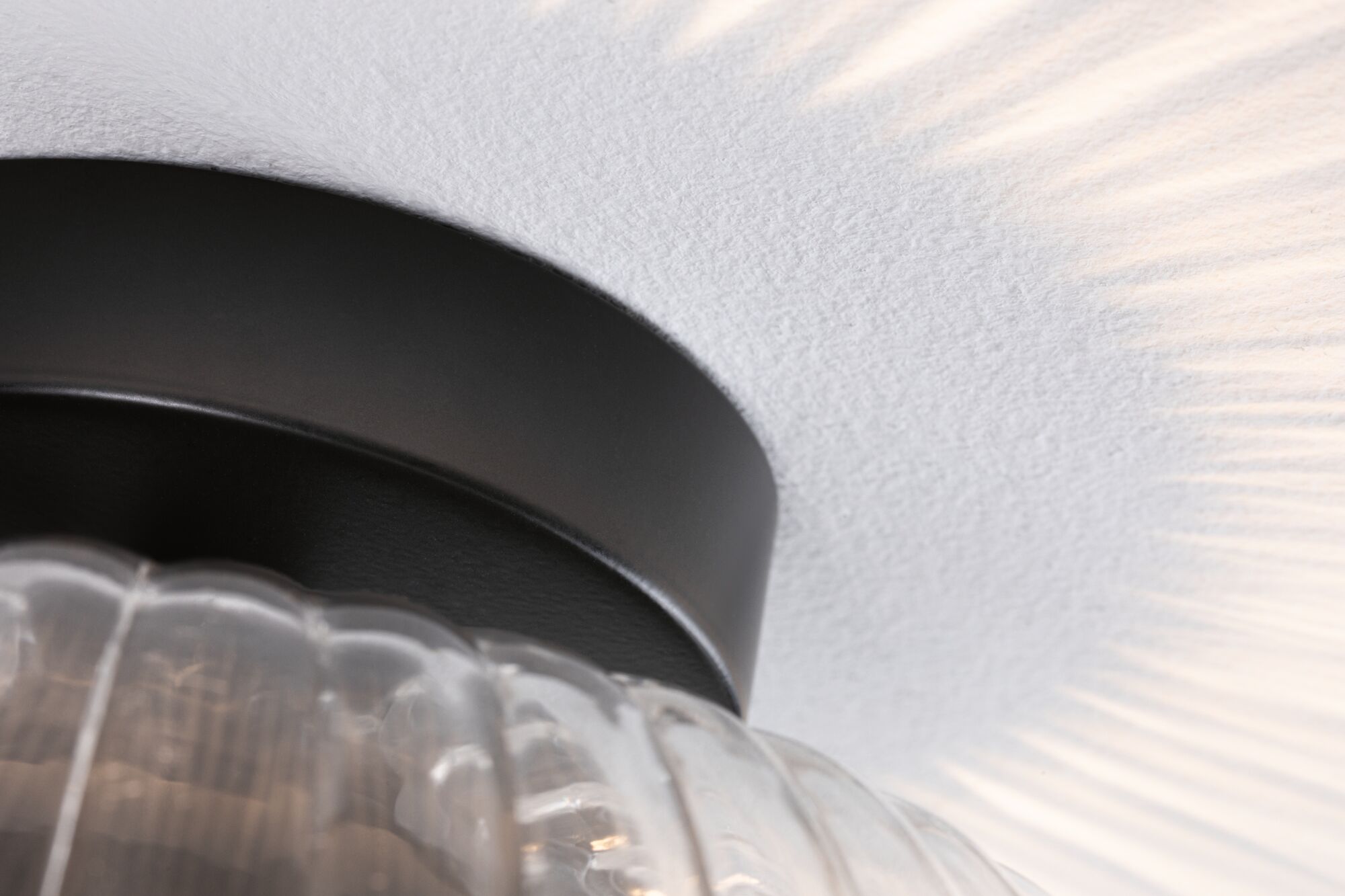 Ceiling light with black metal ring and ribbed clear glass, warm light casting shadow patterns