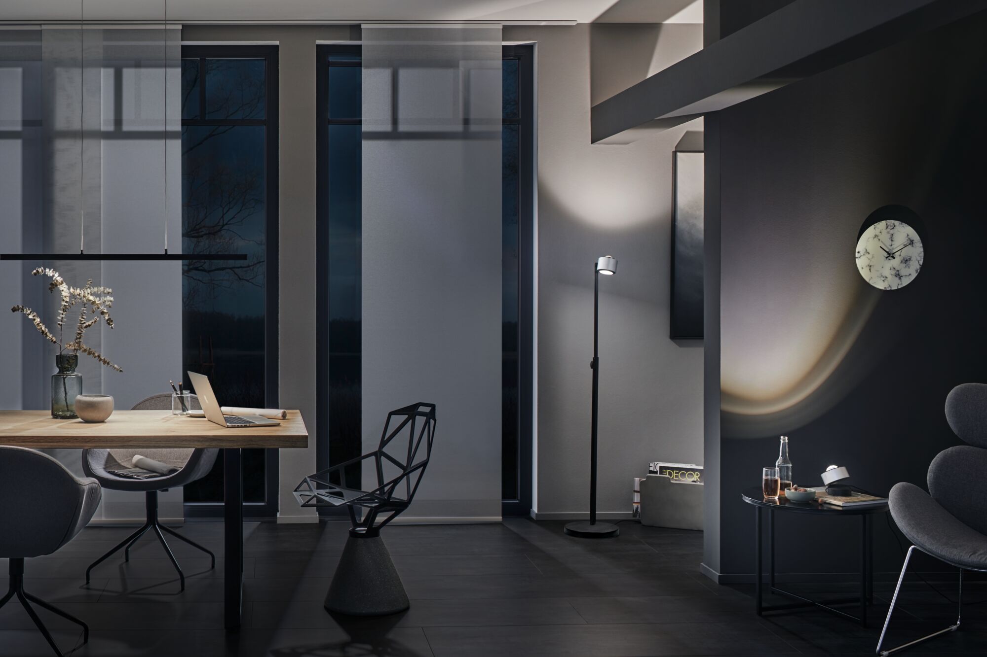 Salon moderne avec lampe sur pied noire, mobilier gris et horloge murale à cadran marbré en lumière tamisée