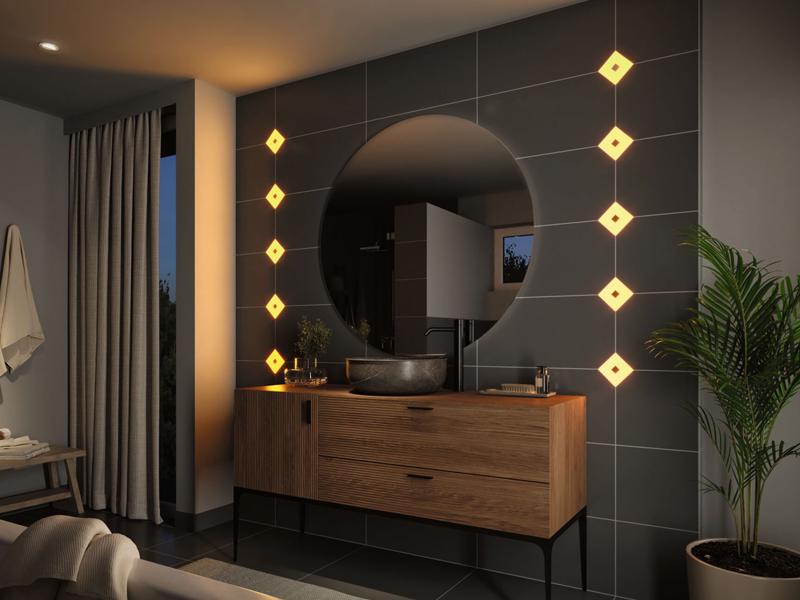 Modern bathroom with warm yellow LED tile lights on dark wall and wooden vanity unit.