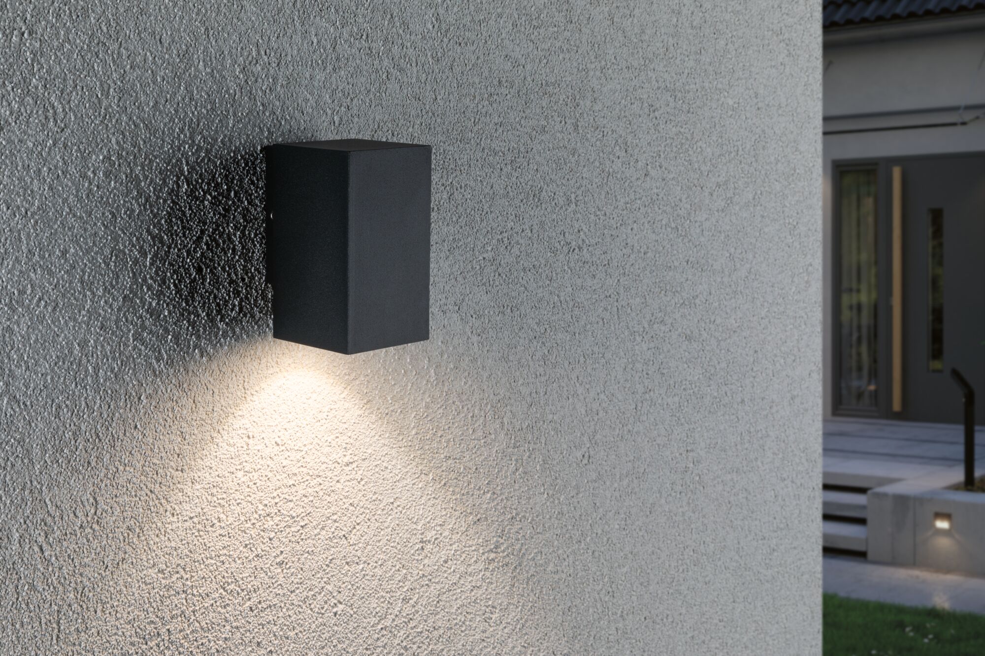 Schwarze rechteckige Außenwandleuchte aus Metall mit warmweißem Licht an grauer Wand