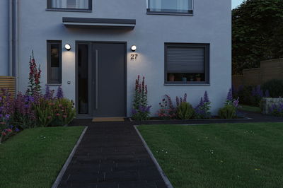 Moderne Hausfassade mit grauer Tür und zwei runden Außenwandleuchten in warmweißem Licht.