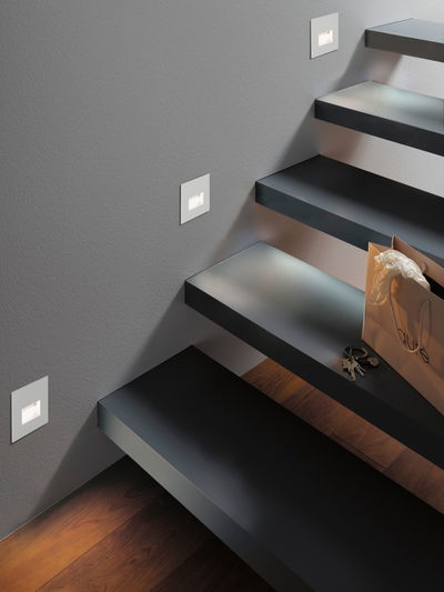 Moderne Treppenbeleuchtung mit weißen LED-Wandeinbauleuchten an grauer Wand und schwarzen Stufen