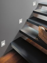 Moderne Treppenbeleuchtung mit weißen LED-Wandeinbauleuchten an grauer Wand und schwarzen Stufen