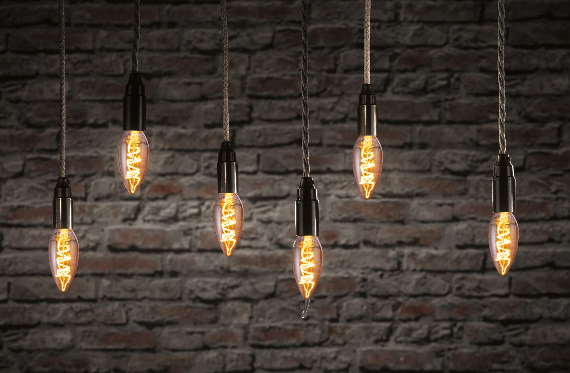 Sechs hängende Vintage-Glühbirnen mit warmem Licht vor roter Backsteinwand, dekorative LED-Beleuchtung