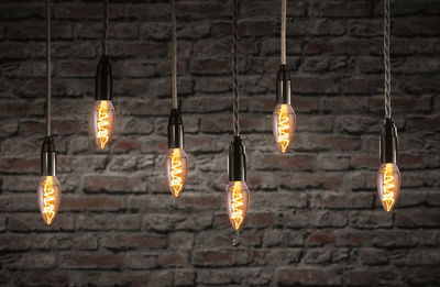 Sechs hängende Vintage-Glühbirnen mit warmem Licht vor roter Backsteinwand, dekorative LED-Beleuchtung