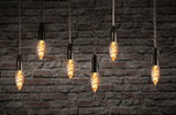 Six hanging vintage filament bulbs with warm light against red brick wall, decorative LED lighting