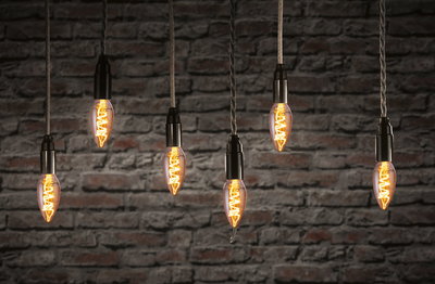 Six hanging vintage filament bulbs with warm light against red brick wall, decorative LED lighting