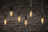 Six hanging vintage filament bulbs with warm light against red brick wall, decorative LED lighting