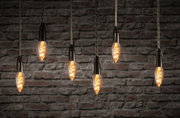 Six hanging vintage filament bulbs with warm light against red brick wall, decorative LED lighting