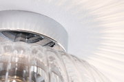 Close-up of clear glass light fixture with chrome metal ring and light reflections on white wall