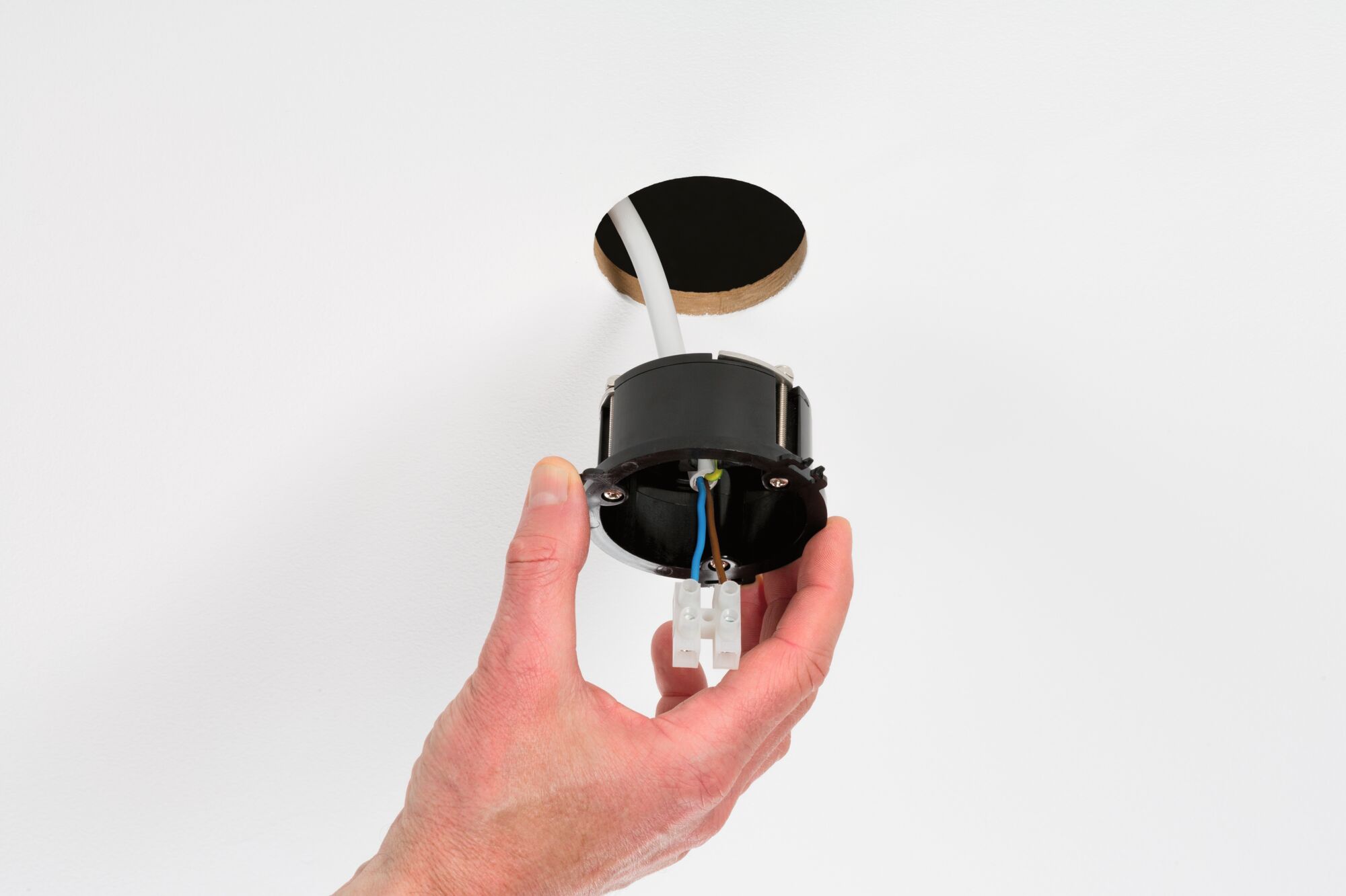 Hand holding black recessed frame with wires near white wall hole for LED downlight installation