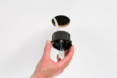 Hand holding black recessed frame with wires near white wall hole for LED downlight installation