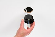 Hand holding black recessed frame with wires near white wall hole for LED downlight installation