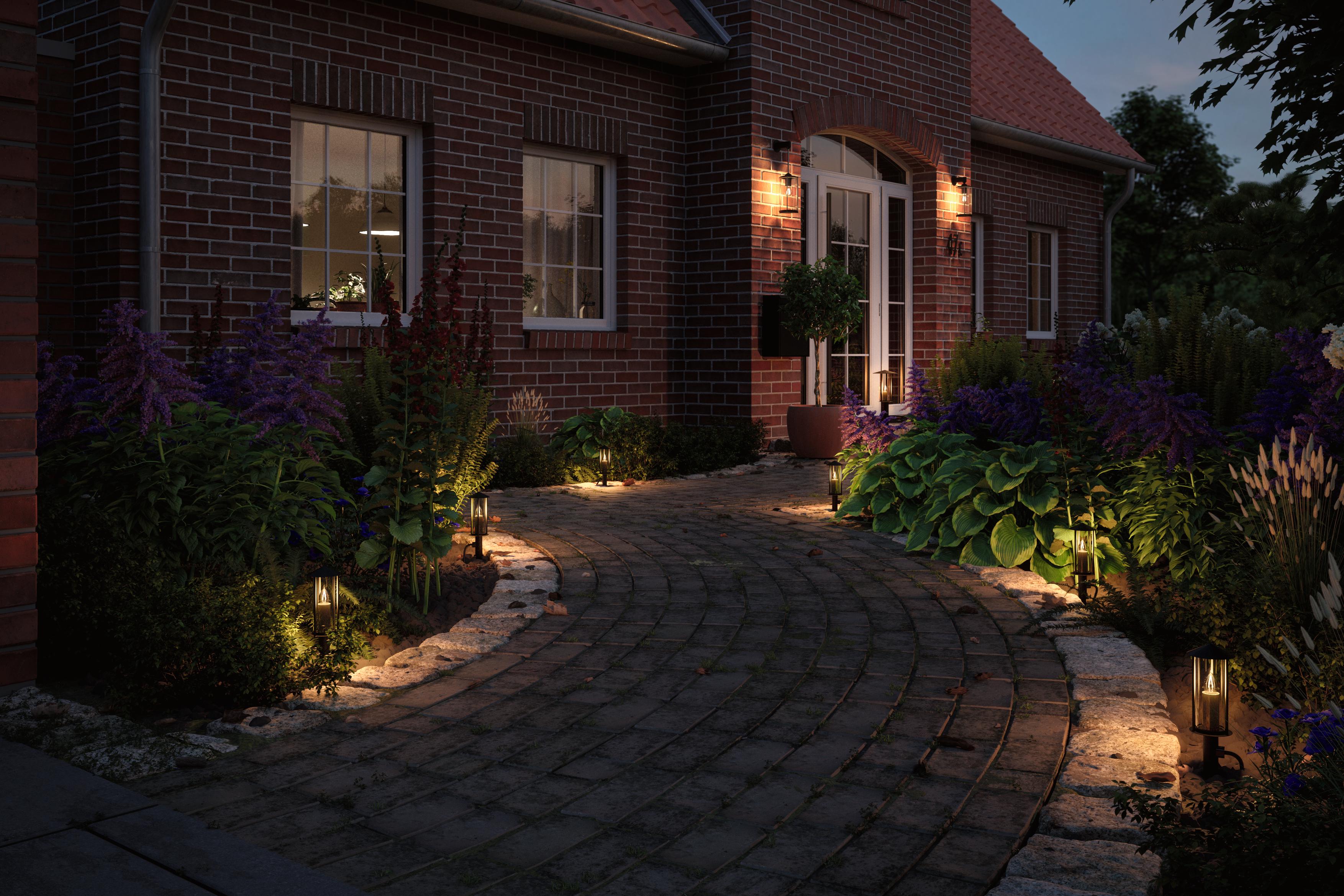 Beleuchteter Gartenweg mit schwarzen Outdoor-Lampen aus Metall und Glas an einem Backsteinhaus.