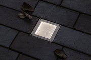 Square recessed LED floor light in stainless steel with warm white glow on dark paving stones